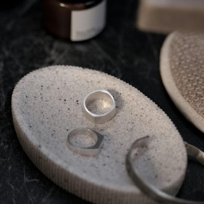 Close-up of minimalist silver jewelry on a textured soap dish, creating a refined still life composition.