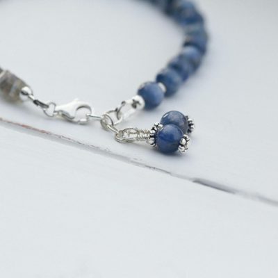 Elegant close-up of a beaded bracelet with blue stones on a white surface, showcasing intricate details.